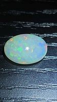 Oval cabochon opal showing green, orange, blue play-of-colour on black background