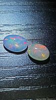 Two oval cabochon opals showing multicoloured play-of-colour on black background