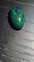 Front view of oval black opal showing green-blue play of colour