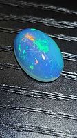 Oval crystal opal showing multicolored fire on black background