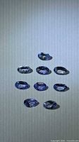 Nine oval blue-violet Tanzanite gemstones laid out on neutral background