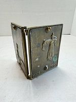 Bi-fold brass frame partially open showing hinged construction and relief figure with Made in Korea mark