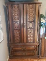 Full view of brown wood veneer armoire with carved doors and bottom drawers