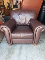 Front view of brown leather armchair with rolled arms and wooden legs