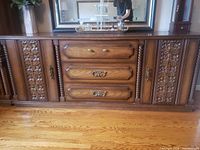 Front view of brown wood veneer dresser showing three drawers, two carved side doors, brass-tone hardware
