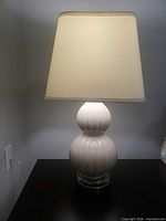 Front view of lamp illuminated showing ceramic body, acrylic base and fabric shade