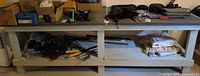Full view of gray painted wood workbench with contents on top and lower shelf