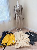 Overall group with trench on mannequin and three other garments on floor