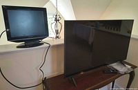 LG 43-inch TV on wooden table with Sharp TV on ledge; remotes and cables visible