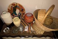 Group view of ceramic vases, orange glass vase, clear glass dishes, woven baskets, textile pieces on table