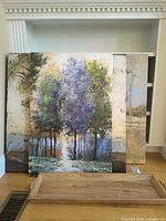 Multiple stacked canvas art panels and wood tray on floor