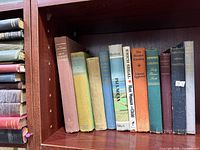 Shelf showing vertical row of assorted vintage hardcovers and horizontal stack of Harvard Classics