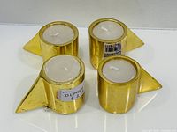 Four gold cylindrical tealight holders with candles