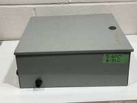 Front/top view of gray steel enclosure showing knockouts, cable gland, plug, lid scuffs