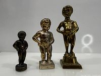Front view of all three Manneken Pis figurines showing relative sizes and finishes