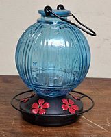 Front view of blue glass hummingbird feeder showing globe, base and red ports