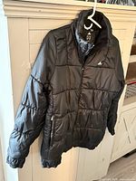 Front view of black Adidas puffer jacket on hanger