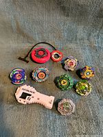 Group shot of eight Beyblade tops, string launcher, ripcord handle, grip and loose forge disc