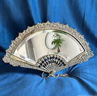 Full front view of brass fan-shaped vanity mirror on blue backdrop