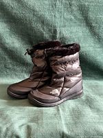Side view of both boots showing quilted upper, faux fur collar, logo, and soles