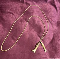 Full view of long gold-tone necklace laid out showing chain and twin fish pendants