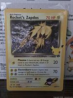 Front of Rocket's Zapdos holo card in sleeve showing artwork, numbering and Pikachu 25th stamp