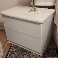 Front and top view of first nightstand showing two drawers and glossy white finish