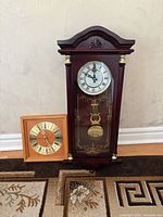 Front view of both clocks on floor: mahogany pendulum clock and oak square clock