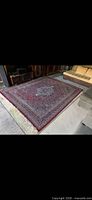 Full view of red oriental rug laid out on floor showing overall pattern and fringe