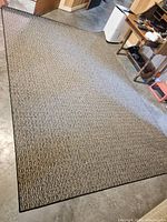 Full view of rectangular beige/tan and black textured loop polypropylene rug spread on concrete floor