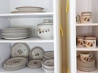 Cabinet shelves showing stacks of dinner and salad plates, lidded casserole, mugs, oval platter
