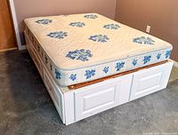 Mattress on platform frame showing floral pattern and frame front drawers