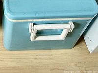 Front side showing teal body and white handle