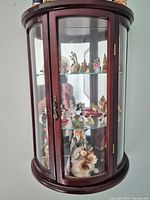 Wall-mounted curved glass cabinet with multiple figurines visible on shelves