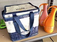 Corona Extra cooler bag beside two Veuve Clicquot bottle carriers