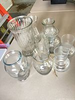 All nine clear glass vases grouped showing varying sizes and textures