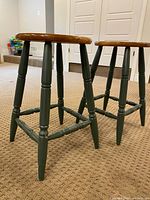 Pair of wooden stools side view showing green painted legs and brown seats