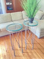 Two metal plant stands with artificial plant displayed beside sofa
