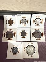 Seven coins in flips laid out showing dates and rusted staples