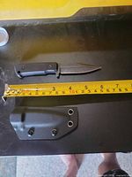 Knife and sheath beside tape measure showing blade and overall length