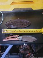 Knife and sheath beside tape measure indicating 8-inch length