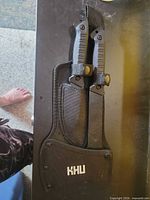 Knife and hatchet secured in nylon sheath with KHU logo visible
