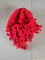 Red crochet balaclava laid flat showing tentacle beard and eye openings