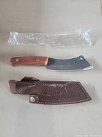 Knife, plastic sleeve, leather sheath laid out