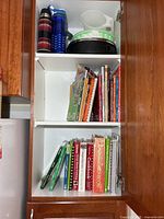 Cupboard showing cookbooks on two shelves and kitchen items on upper shelf