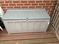 Front view of grey resin deck box against brick wall