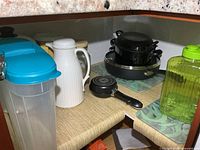 Interior of cupboard showing saucepans, insulated carafe, cereal container, green jug