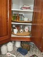 Cabinet shelves showing canister set, colored tumblers, clear mugs, sugar bowl, creamers, tea cozies, spoon rest, napkins