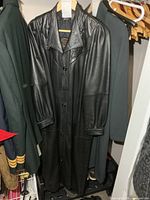 Full view of long black leather coat hanging in closet