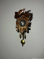 Front view of carved wood cuckoo-style clock showing dial, bird and leaf carvings